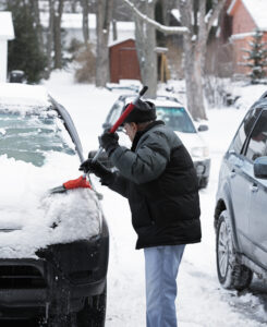 Man outside in winter brushing snow off a car