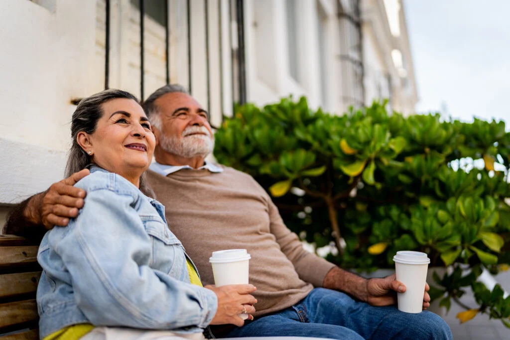 Senior couple looking away sitting on a bench outdoors with coffee