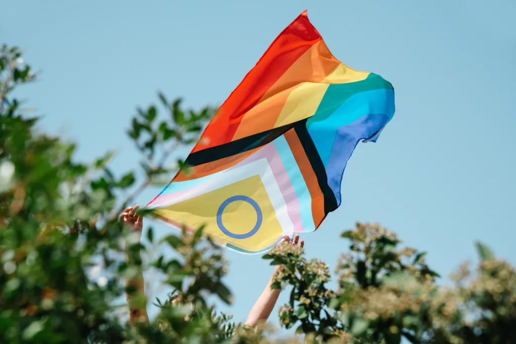 Progress Pride flag held up against a blue sky.